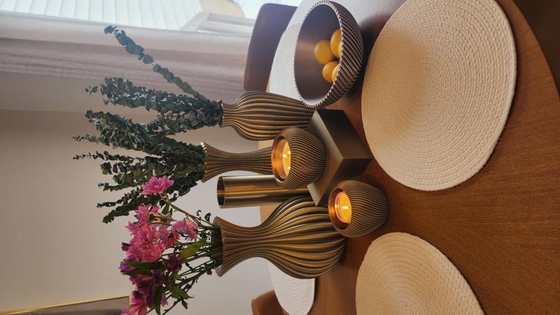 Black and gold ridged vases with flowers and candle on dining table
